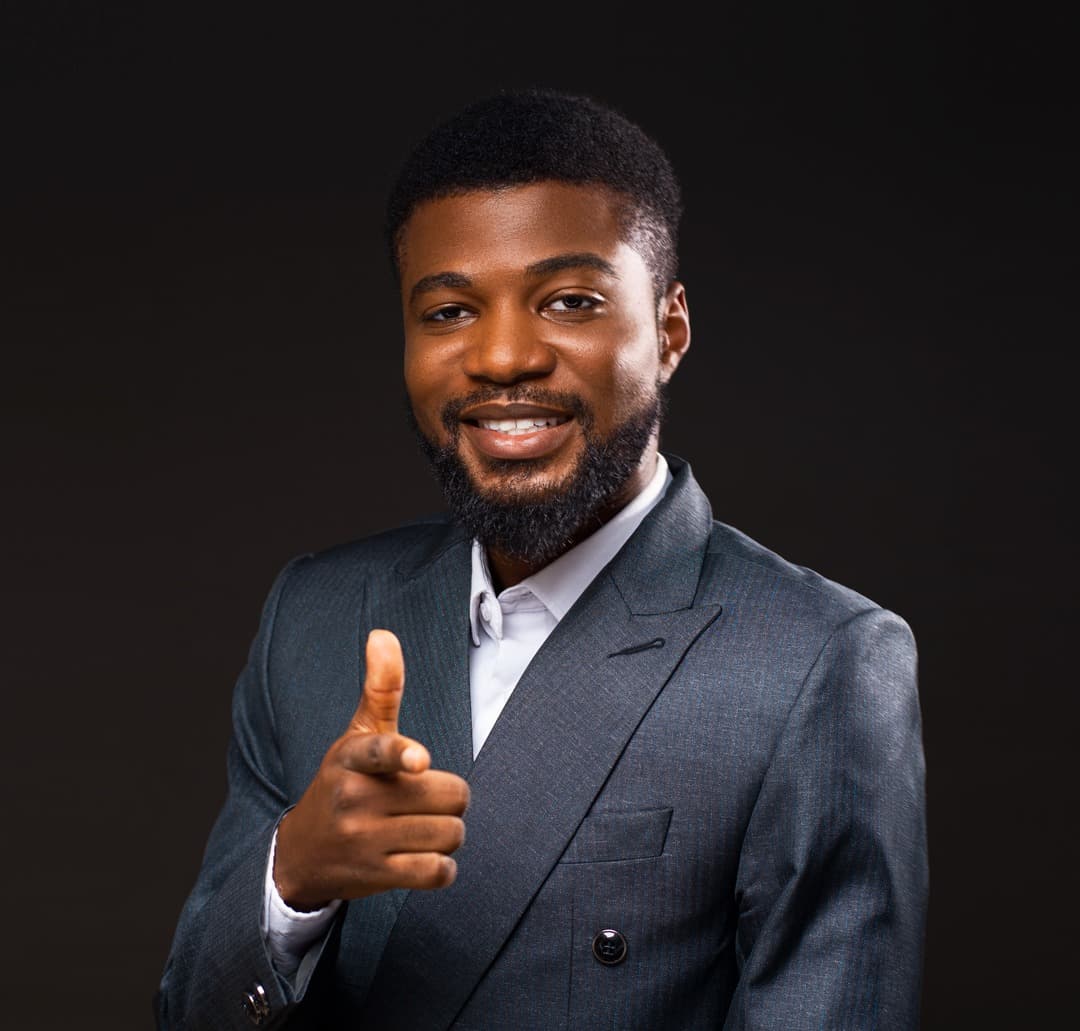 ’Joba Ojelabi in a grey suit, smiling and pointing